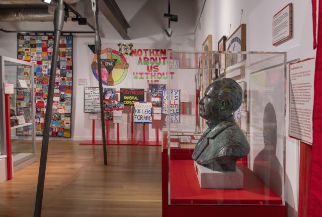 Disability activism protest signs and a bust of Francis Maginn are visible inside a museum.